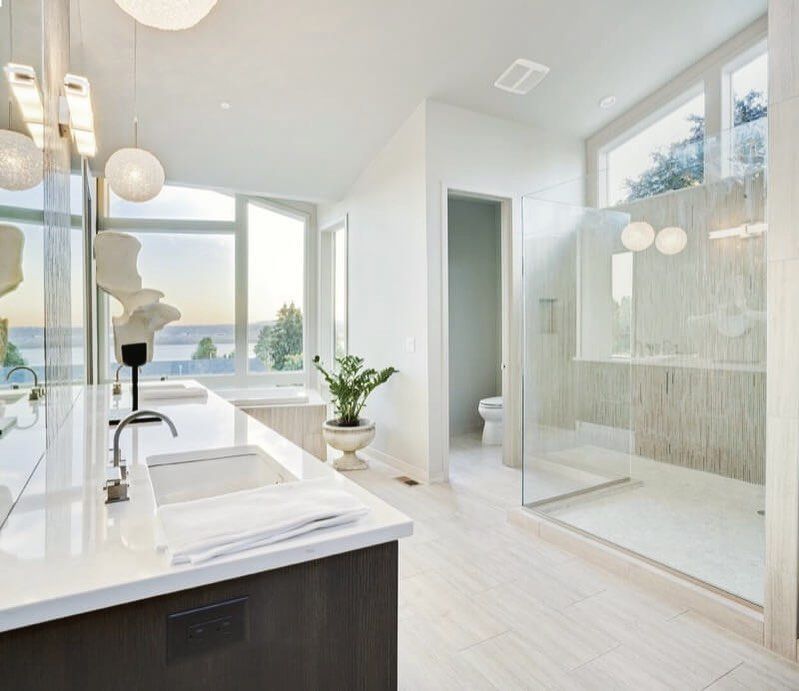 Modern white bathroom with large windows, shower, and double vanity.