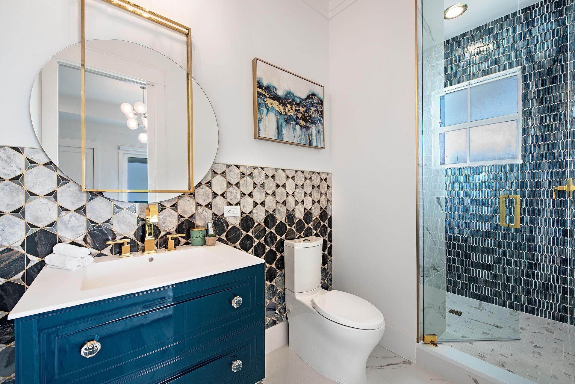 Elegant bathroom with teal vanity, patterned tile, gold accents, and glass shower.