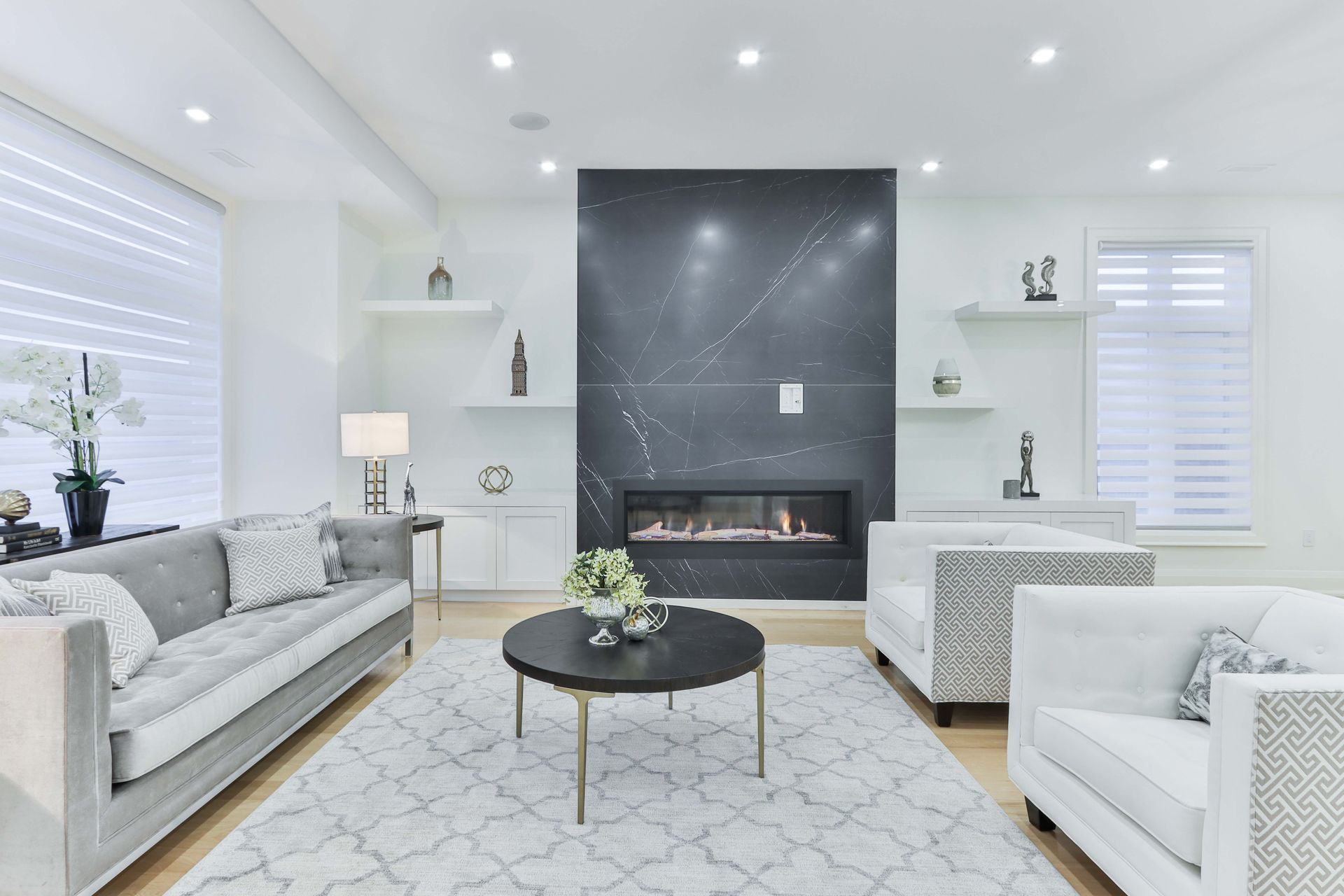 Living room with gray sofa, white chairs, black fireplace, and light wood floors.