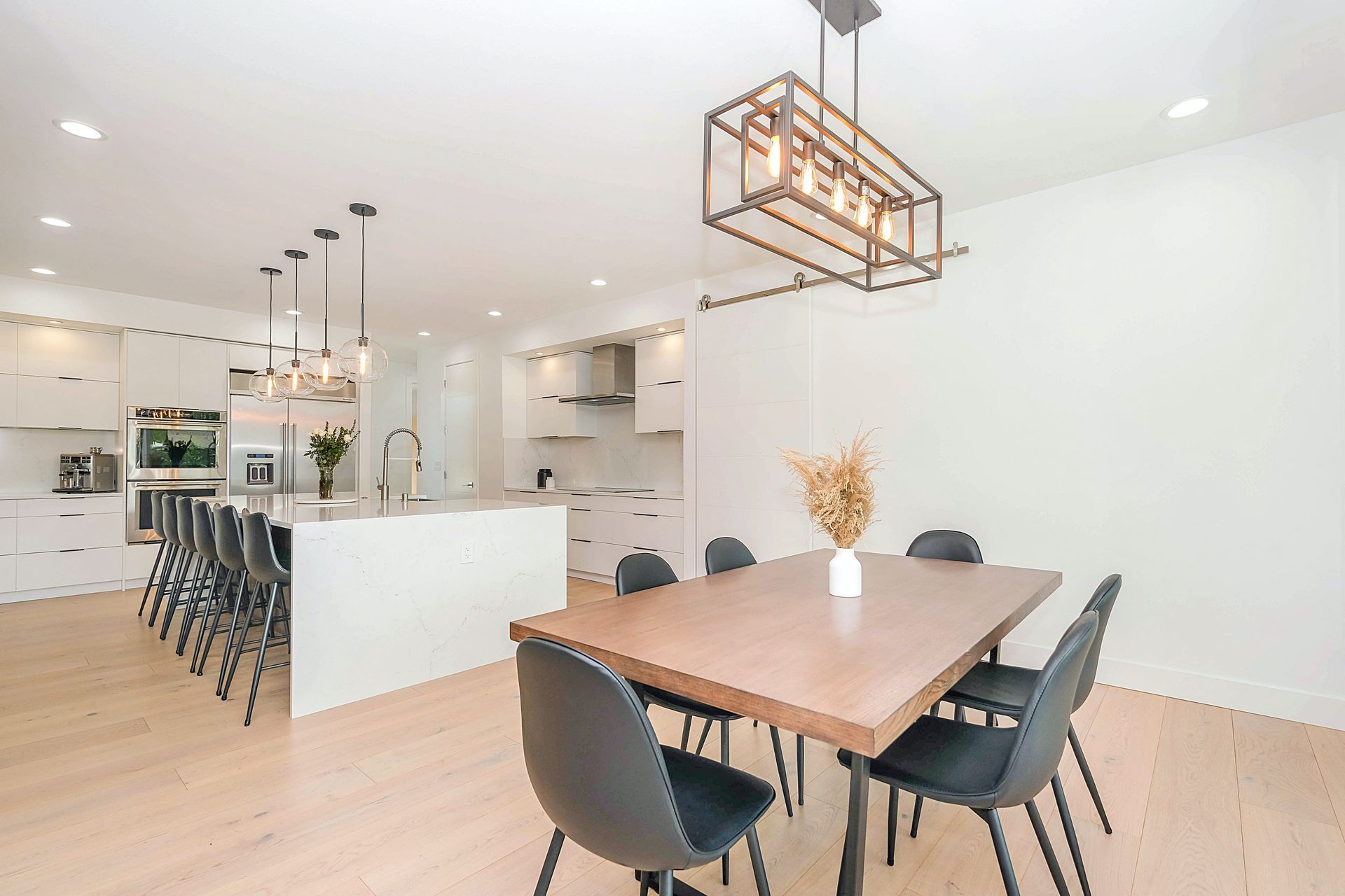 Modern open-concept dining area with kitchen: wooden table and black chairs, white cabinets, and wooden floors.