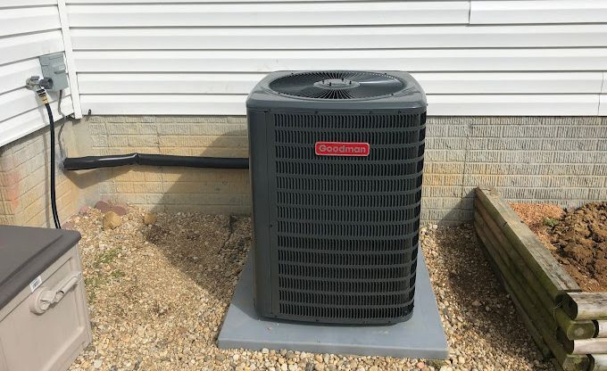 Goodman air conditioning unit outside a house, on a concrete pad.