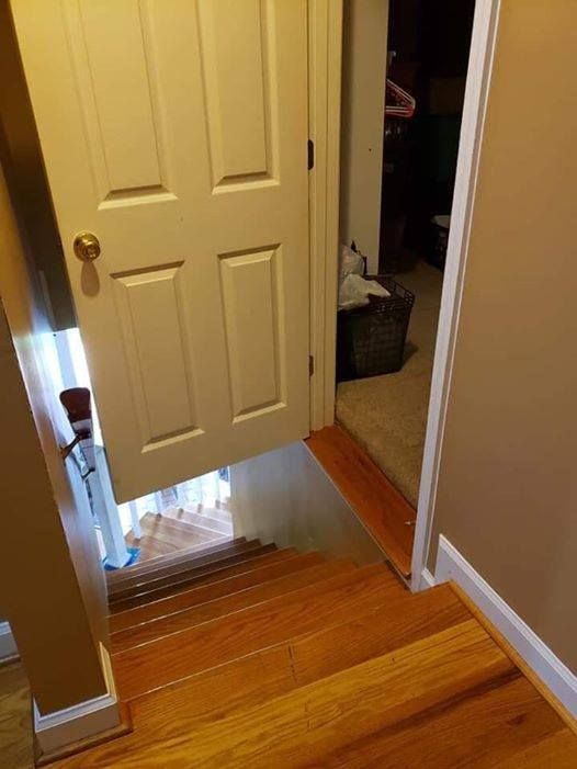 Partially open white door at top of a wooden staircase, revealing a hallway beyond