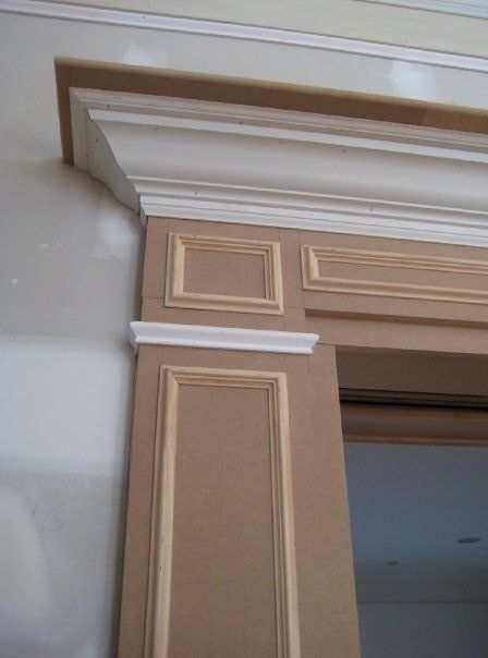 Decorative beige and white crown molding around a doorway in an interior room
