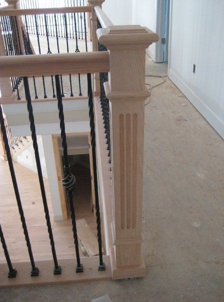 Staircase landing with a beige wooden post and black metal railing beside a hallway opening