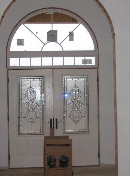 Double front doors with decorative glass in a white arched entryway, with a box on the floor
