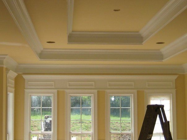 Cream-colored room with tray ceiling, large windows, and a ladder near the right wall.