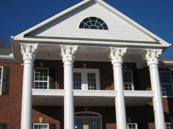 White-columned brick building with a portico and arched window under a blue sky