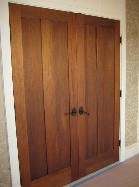 Wooden double closet doors with dark handles in a hallway, framed by patterned wallpaper