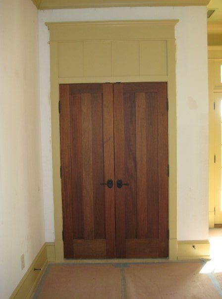 Wooden double doors in a hallway with white trim and warm lighting