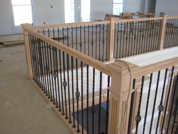 Interior stairwell with beige wood railings and black metal balusters around an open landing