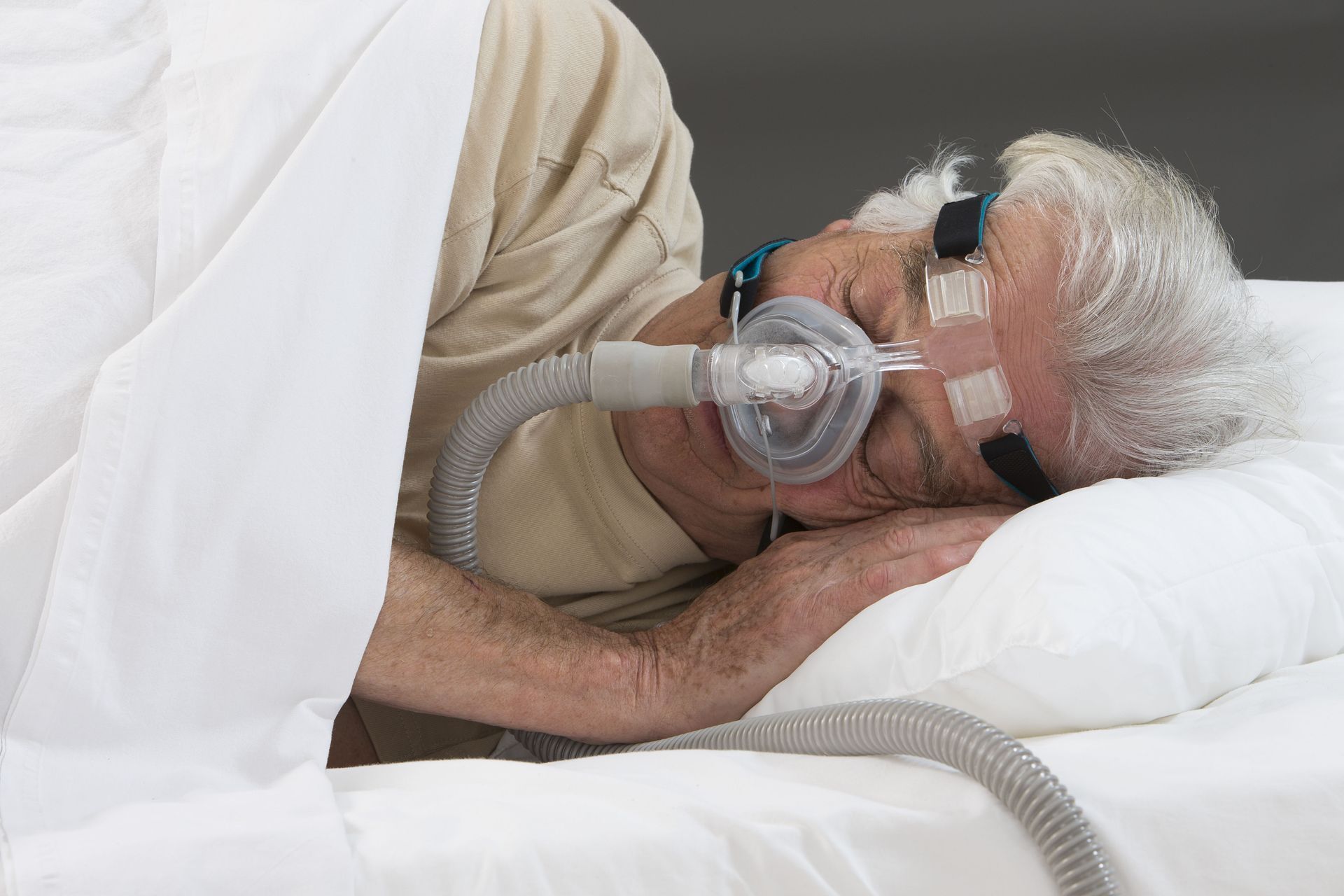 An elderly man is sleeping in a bed with an oxygen mask on his face.