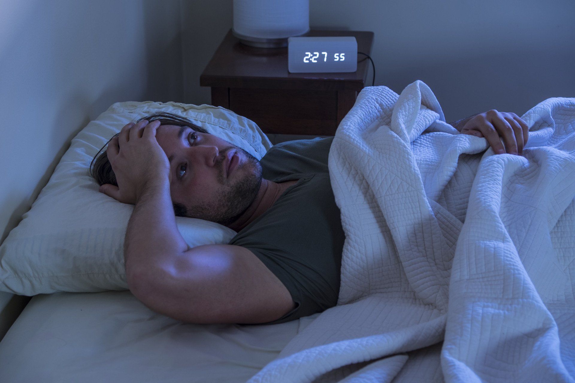 A man is laying in bed with his hand on his head.