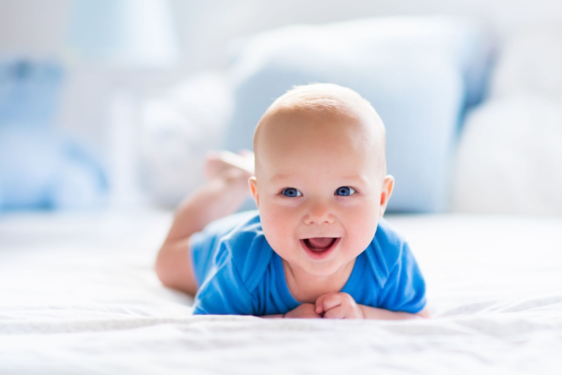 A baby is laying on his stomach on a bed and smiling.