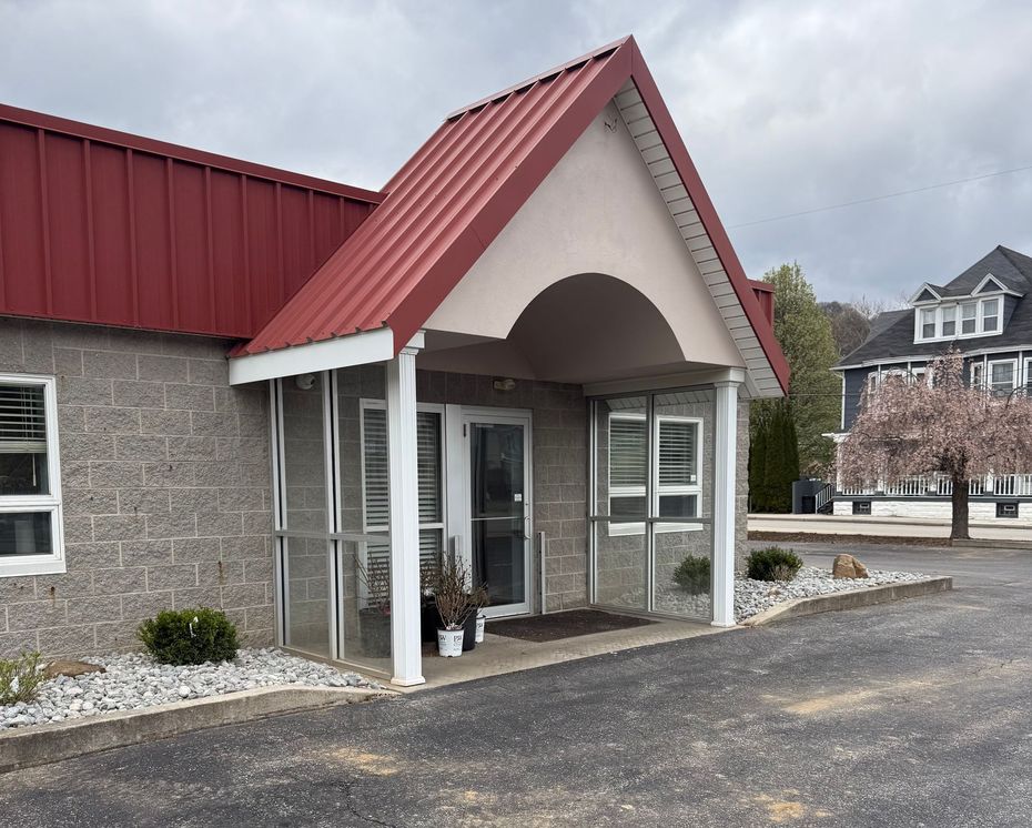 Building entrance with a red roof, stone facade, and white columns under a cloudy sky.