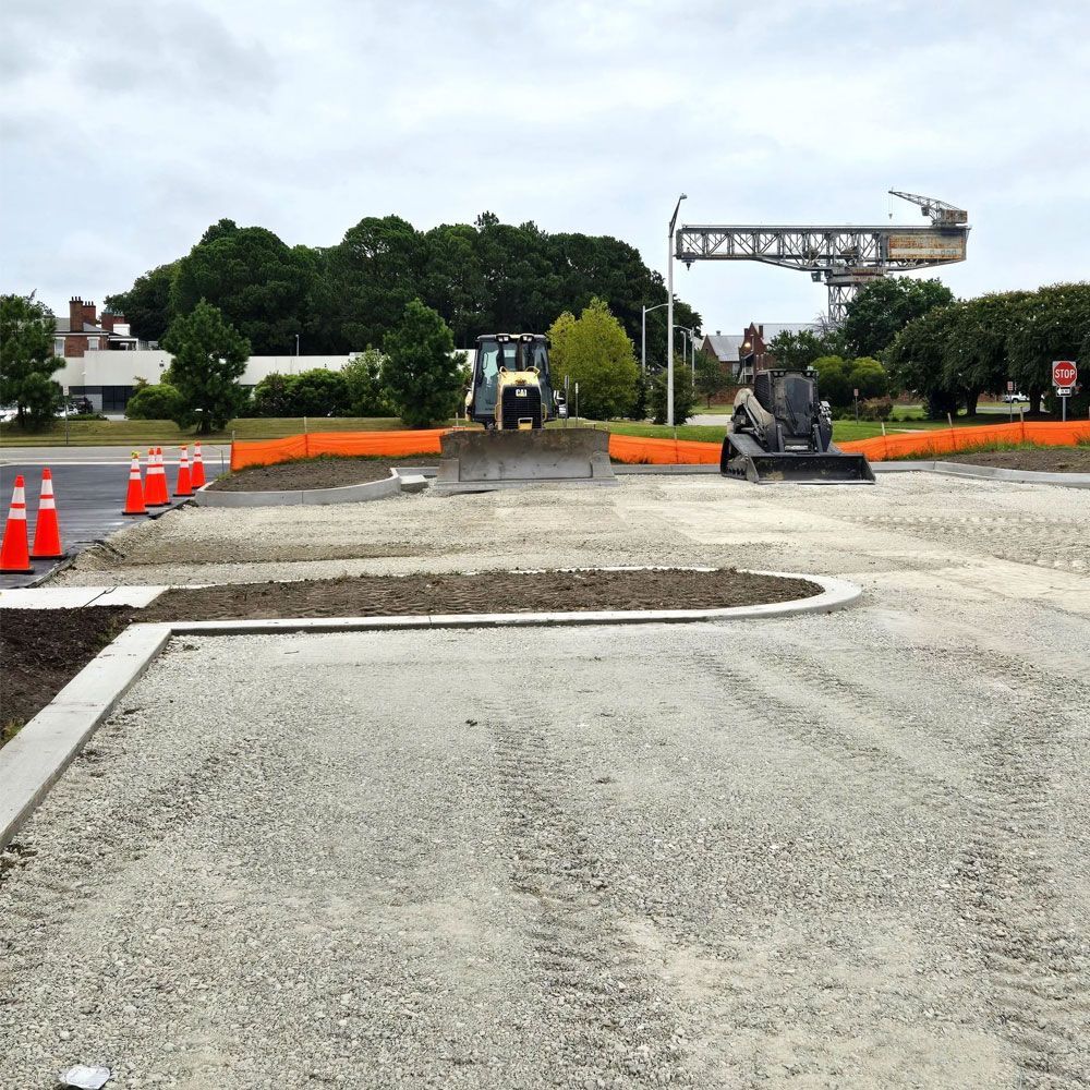 Construction site with gravel ground, orange safety fencing, construction equipment, and a large crane in the background.