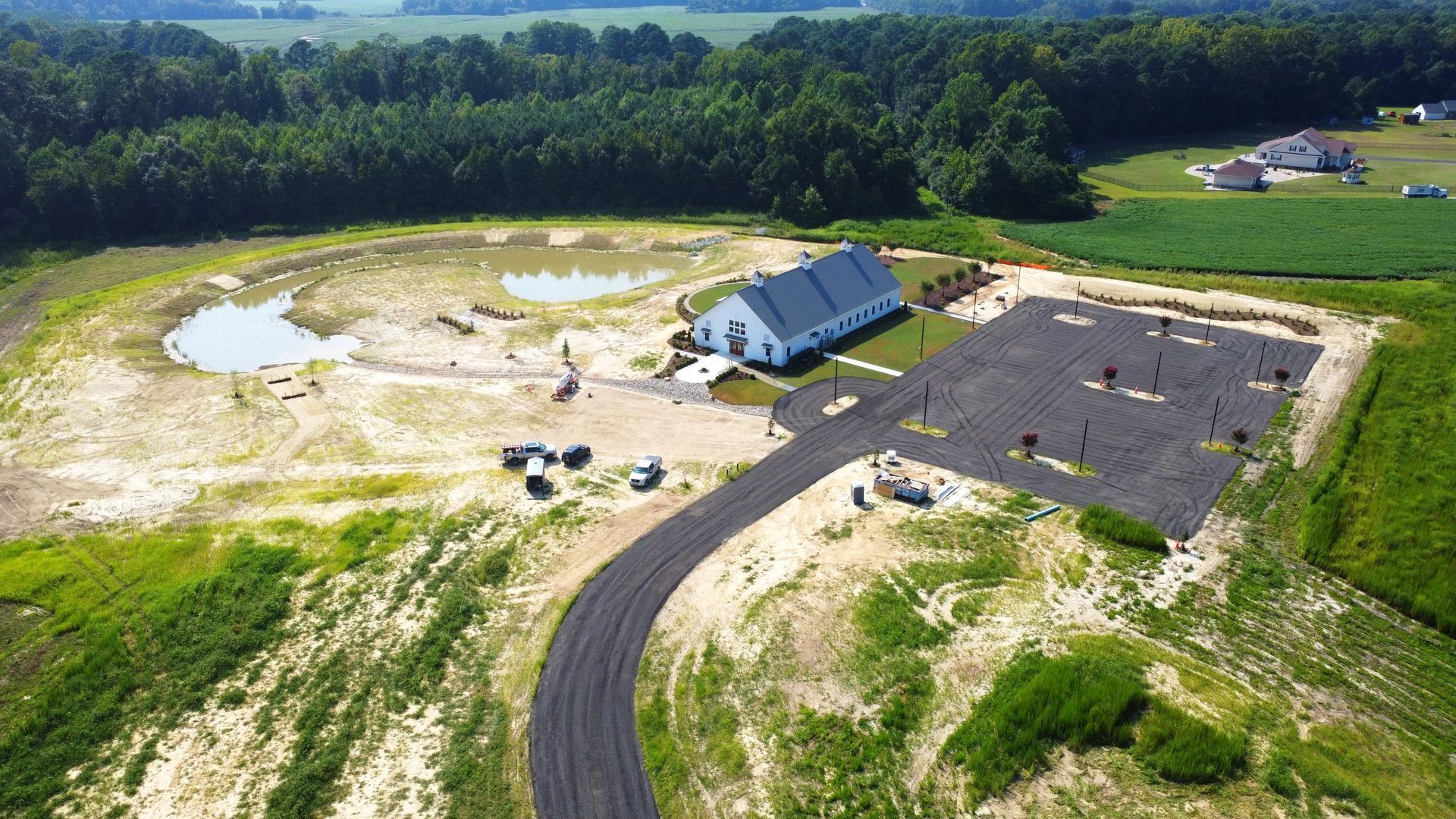 Aerial view of a white house with a paved driveway and parking lot, next to an unlandscaped yard with small ponds.