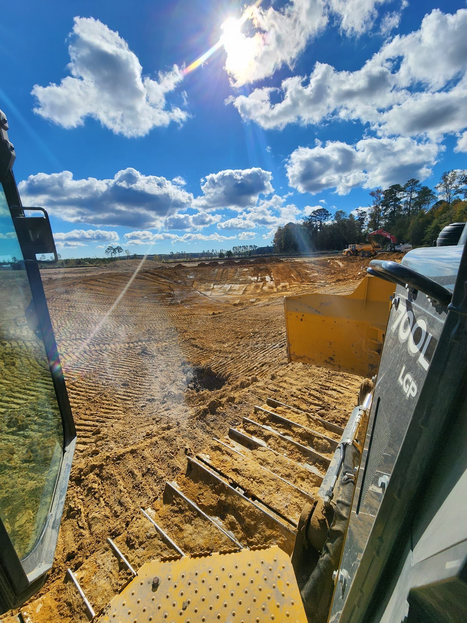 A first-person view from inside heavy construction equipment overlooking a cleared, dirt-covered site under a blue sky.