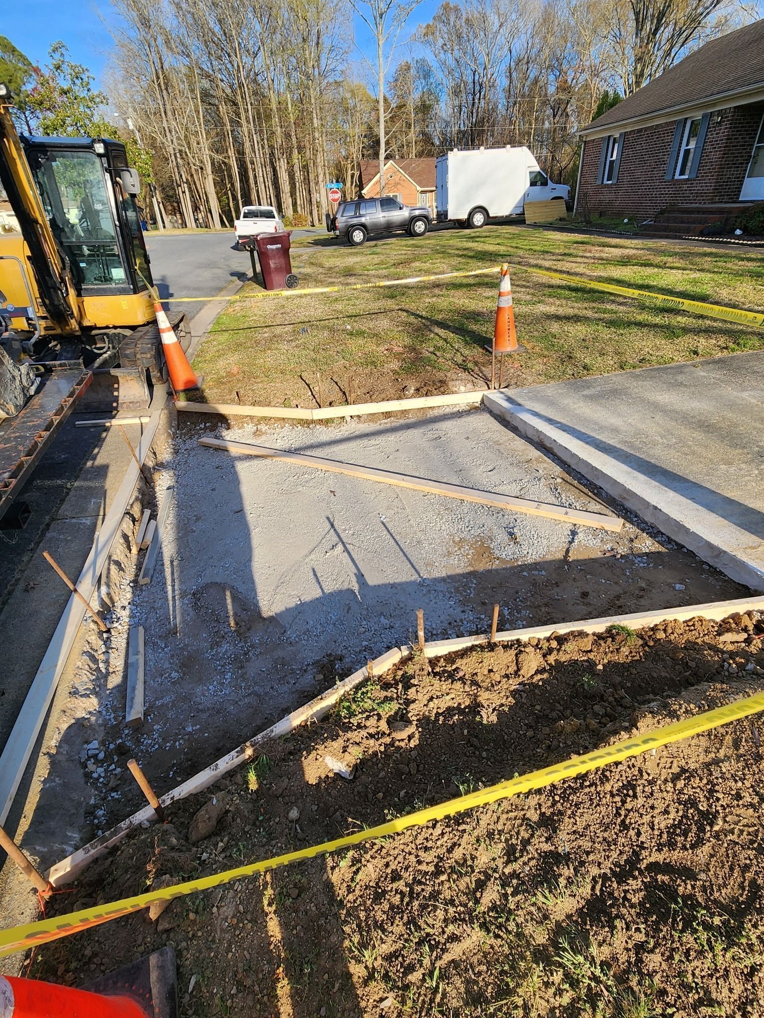 Construction site showing a prepared, gravel-filled driveway section framed with wood forms for a concrete pour.