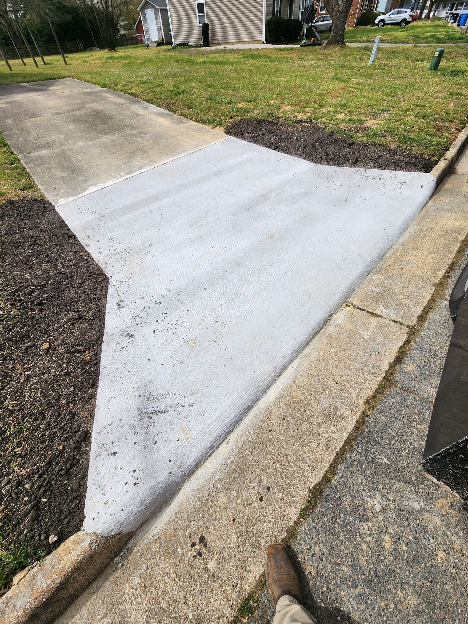 A newly poured concrete driveway apron connecting a sidewalk to a paved driveway, surrounded by landscaping.