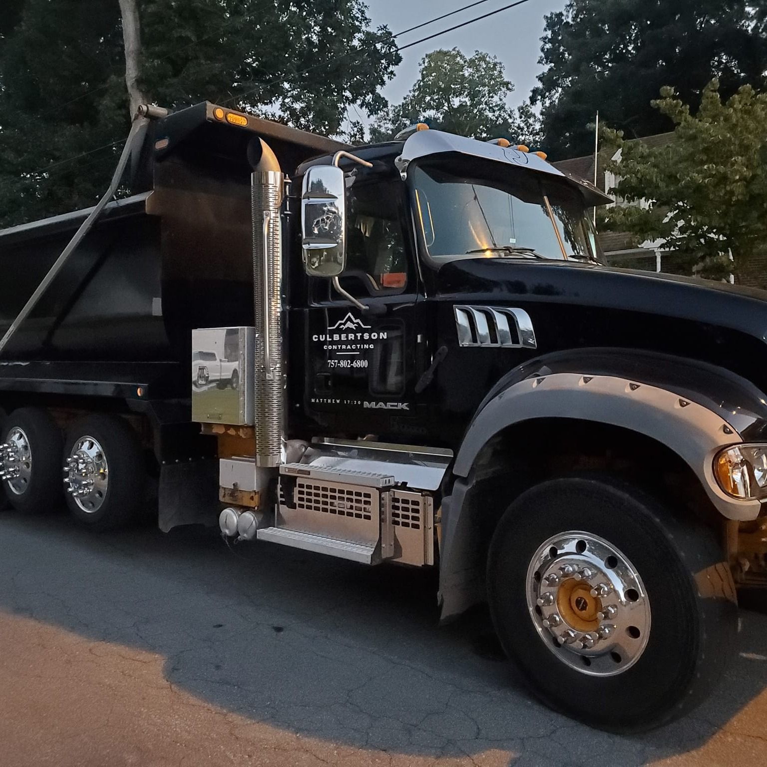 A black Mack dump truck parked on an asphalt street with chrome trim and wheels visible.