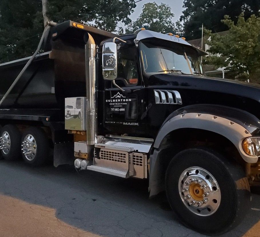A black Mack dump truck with chrome accents and a logo on the door is parked on an asphalt surface at dusk.