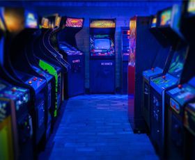 A dimly lit, blue-tinted arcade aisle lined with rows of vintage video game cabinets.