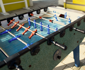 A foosball table with red and blue player figures on metal rods, set outdoors on a paved surface.