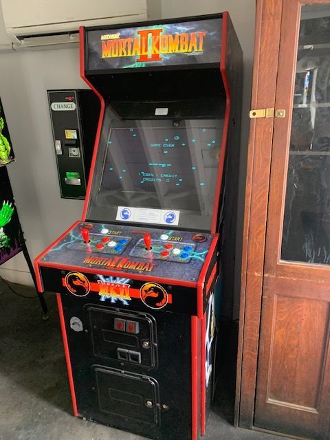 Black arcade game cabinet with red trim in a hallway beside a wooden door.