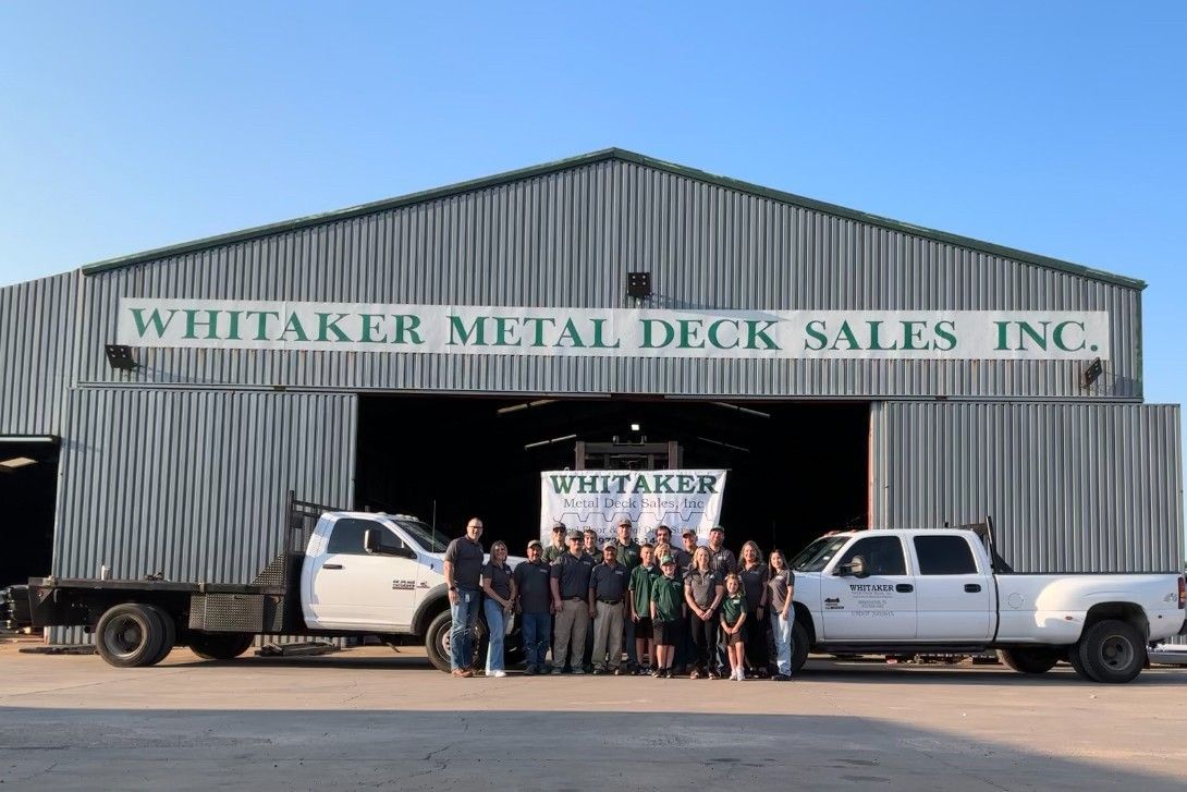 Whitaker Metal Deck Sales Inc. employees pose with trucks in front of their corrugated metal warehouse.