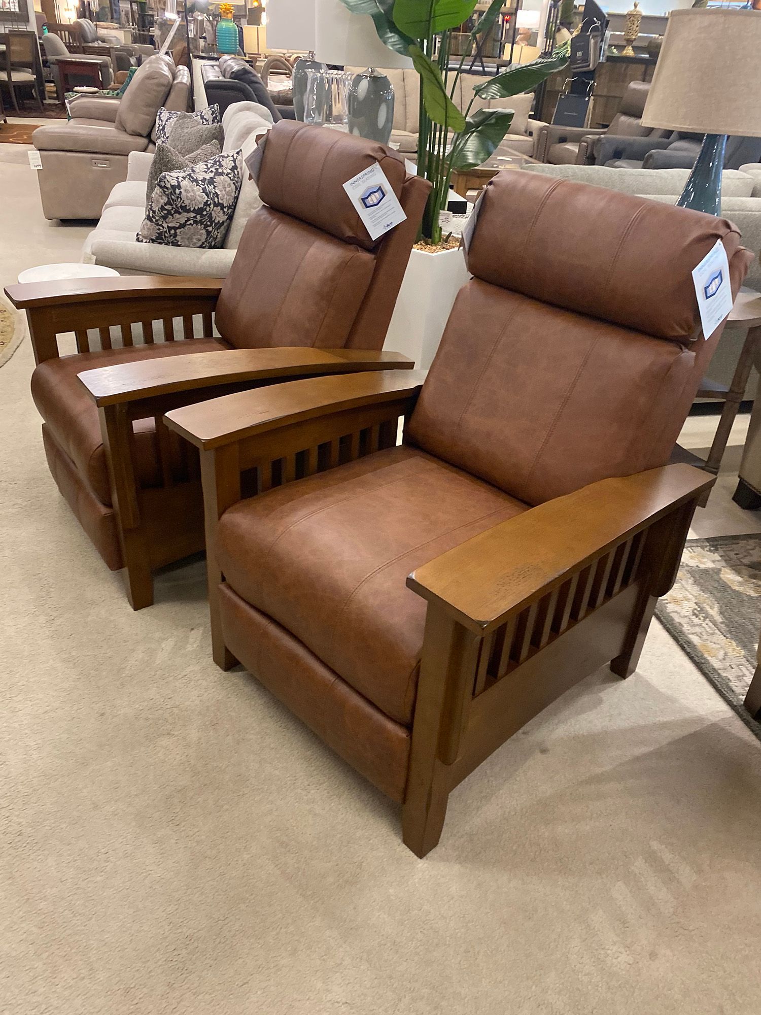 Two brown leather recliner chairs with wooden armrests in a furniture store.