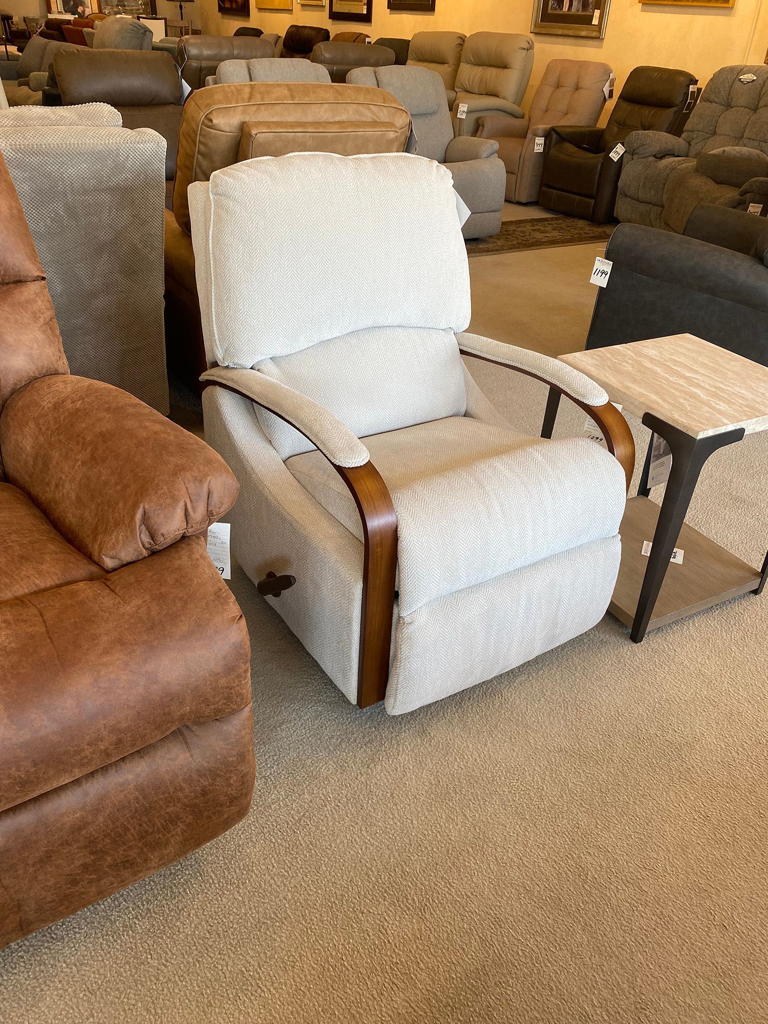 White recliner with wooden armrests, next to a small table; inside a furniture store.