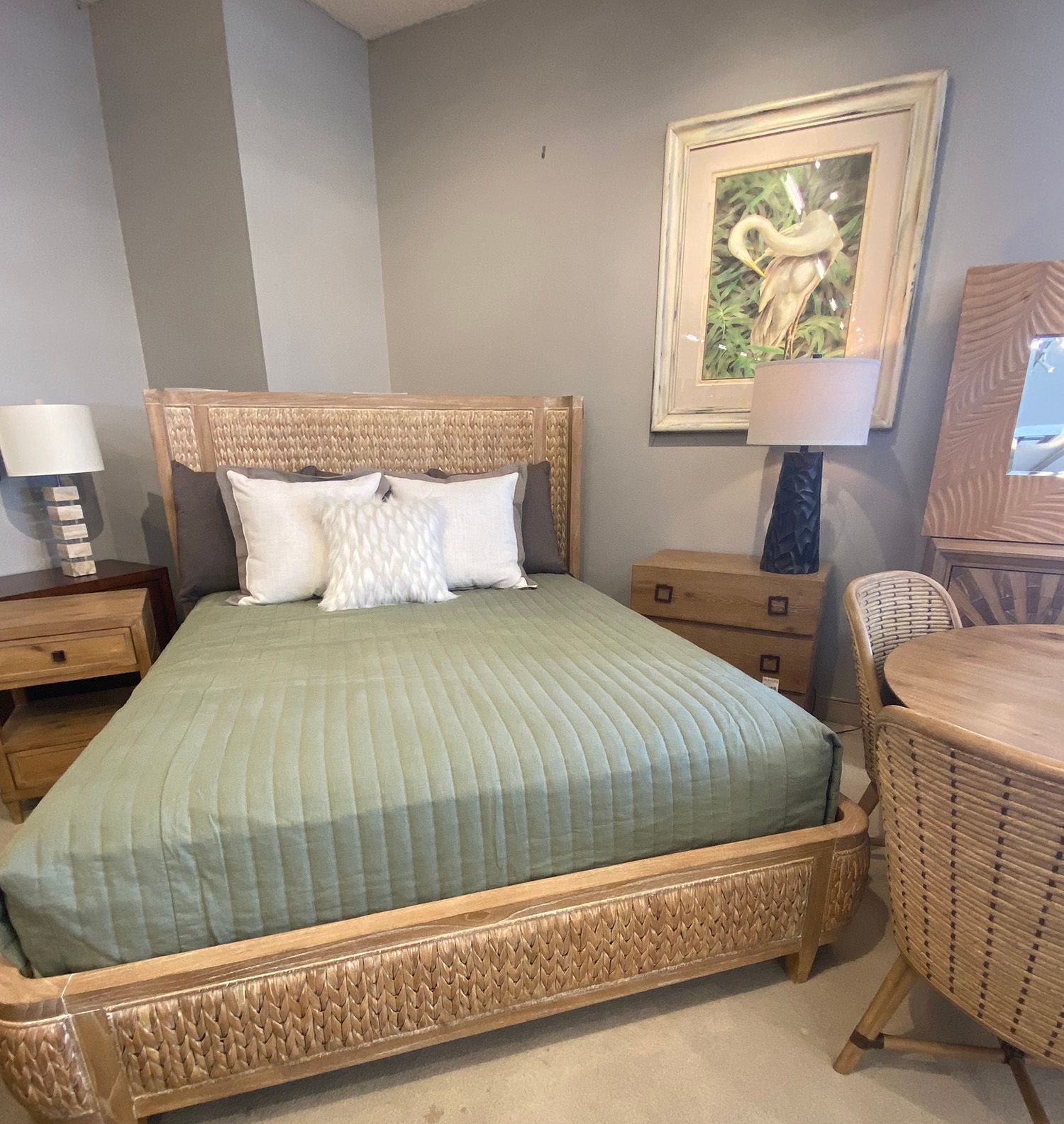 Bedroom with rattan bed, green quilt, wooden nightstand, art, and lamp.