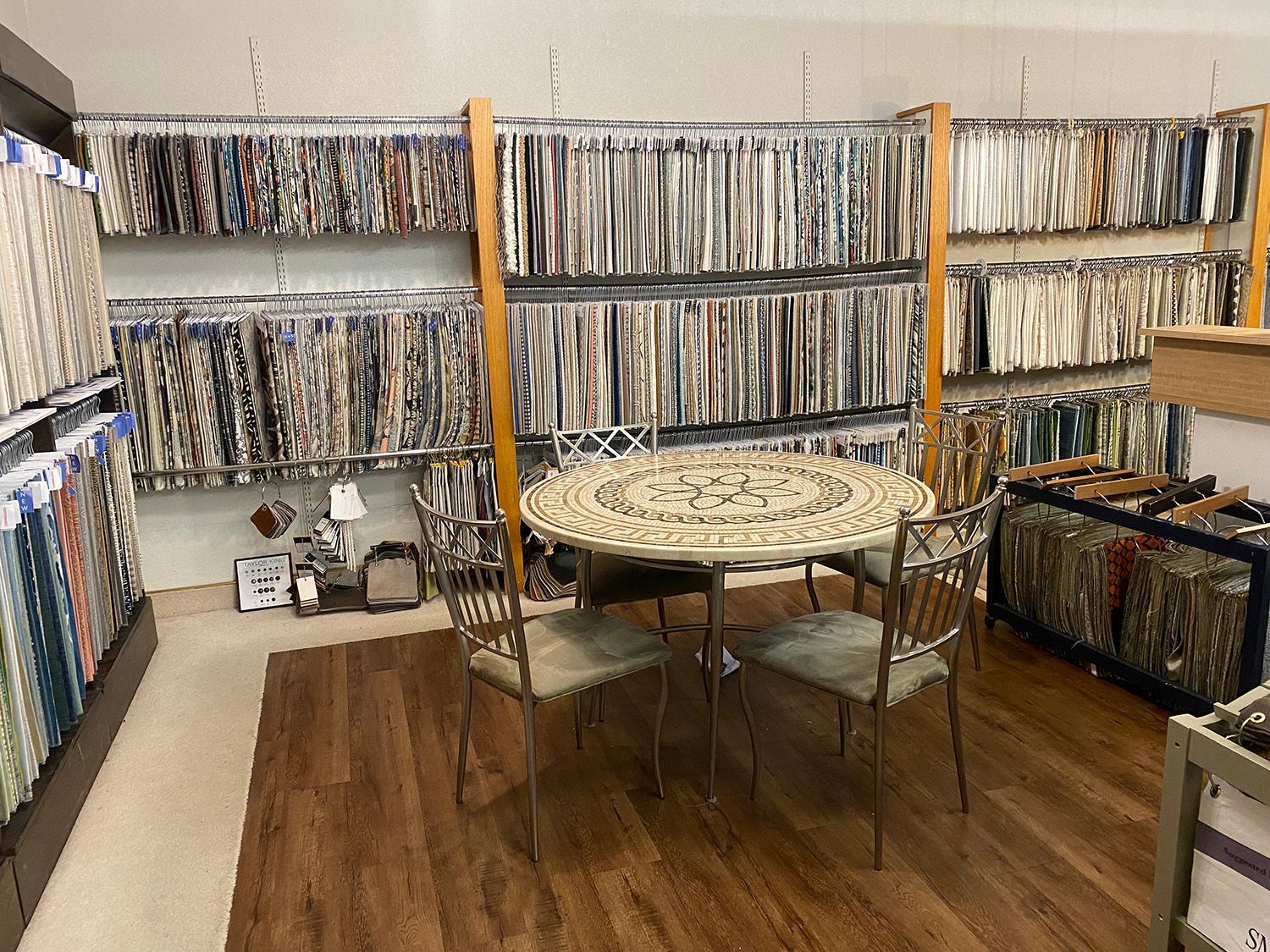 Fabric store display with round table and chairs surrounded by fabric samples. Wooden floors.
