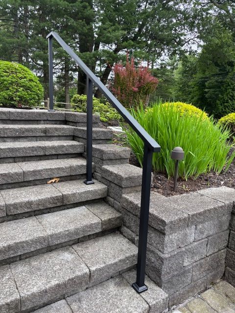 Accessible outdoor stone stairway with black handrail beside a landscaped garden