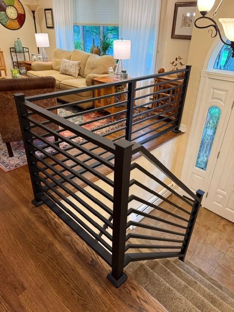 Black metal railing around a staircase in a living room with wood floors and beige furniture.