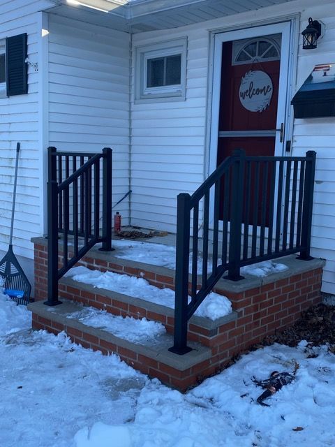 Front porch with black railings, brick steps, and a red door in snowy weather