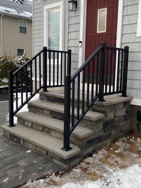 Front steps to a house with black railings, gray stone stairs, and a red front door.