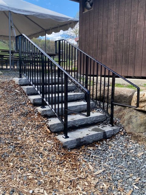 Black metal handrail and concrete steps beside a wooden building under a canopy.