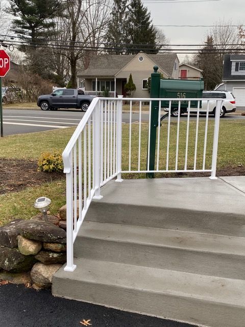 Concrete steps with white railing leading to a sidewalk beside a street and parked vehicles