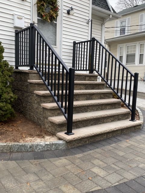 Front steps with black railings leading to a house entrance and stone-paved walkway