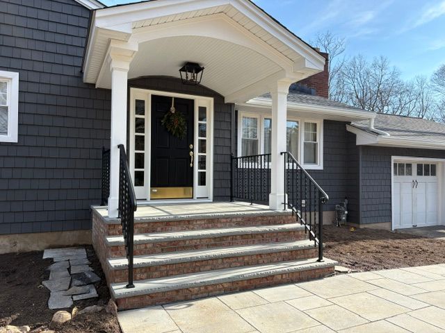 Front porch entrance with black railings, brick steps, white trim, and a garage beside it