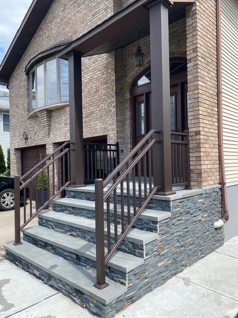 Brick townhouse entrance with gray stone steps, brown railings, and a covered front door.