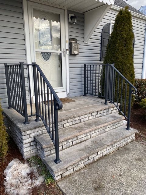 Front steps with black railings leading to a white front door of a gray house.