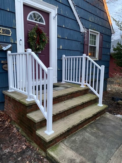 Front porch steps with white railings leading to a red front door on a blue house
