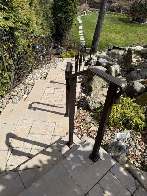 Stone steps with black handrails descending through a landscaped garden toward a grassy path