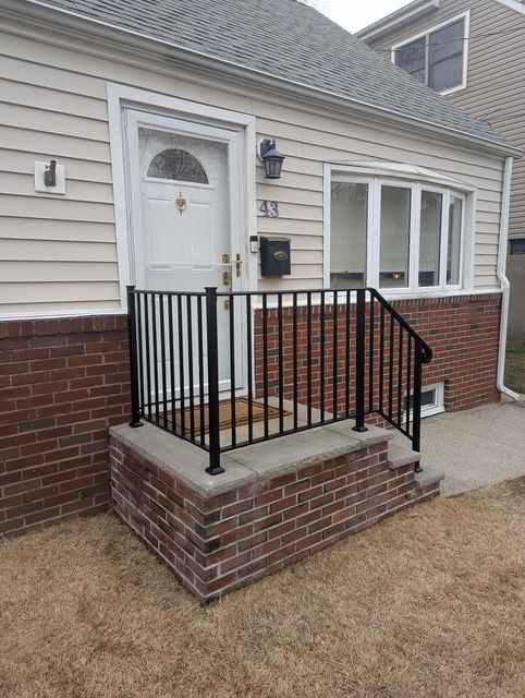 Front entrance of a house with brick steps, black railings, white door, and beige siding