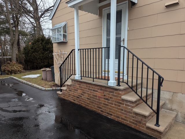 Brick front steps with black railings leading to a beige house entry.
