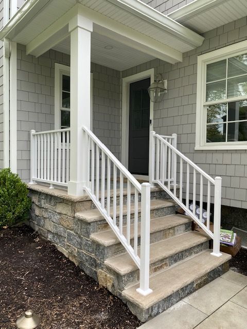 Front porch steps with white railings and stone foundation at a house entrance