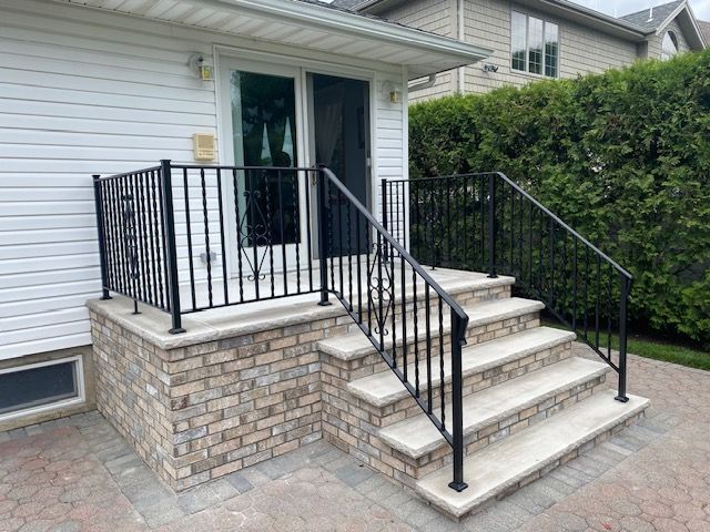 Front porch with stone steps, black railings, and a white door on a house exterior