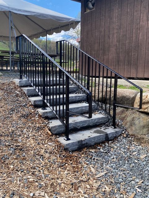 Outdoor concrete steps with black railings leading up beside a brown building under a canopy.
